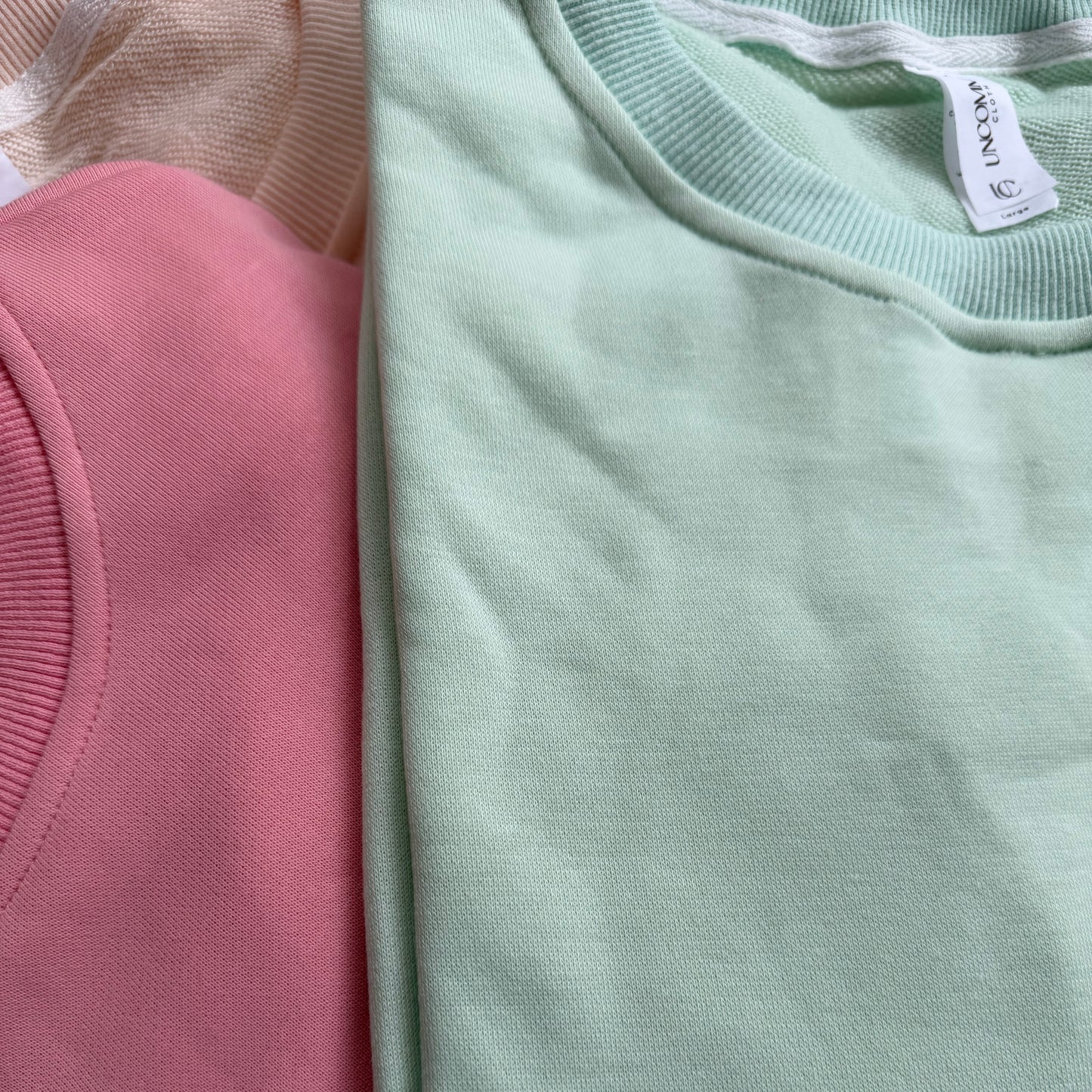 Close-up of pink and green sweatshirts with a brand tag.