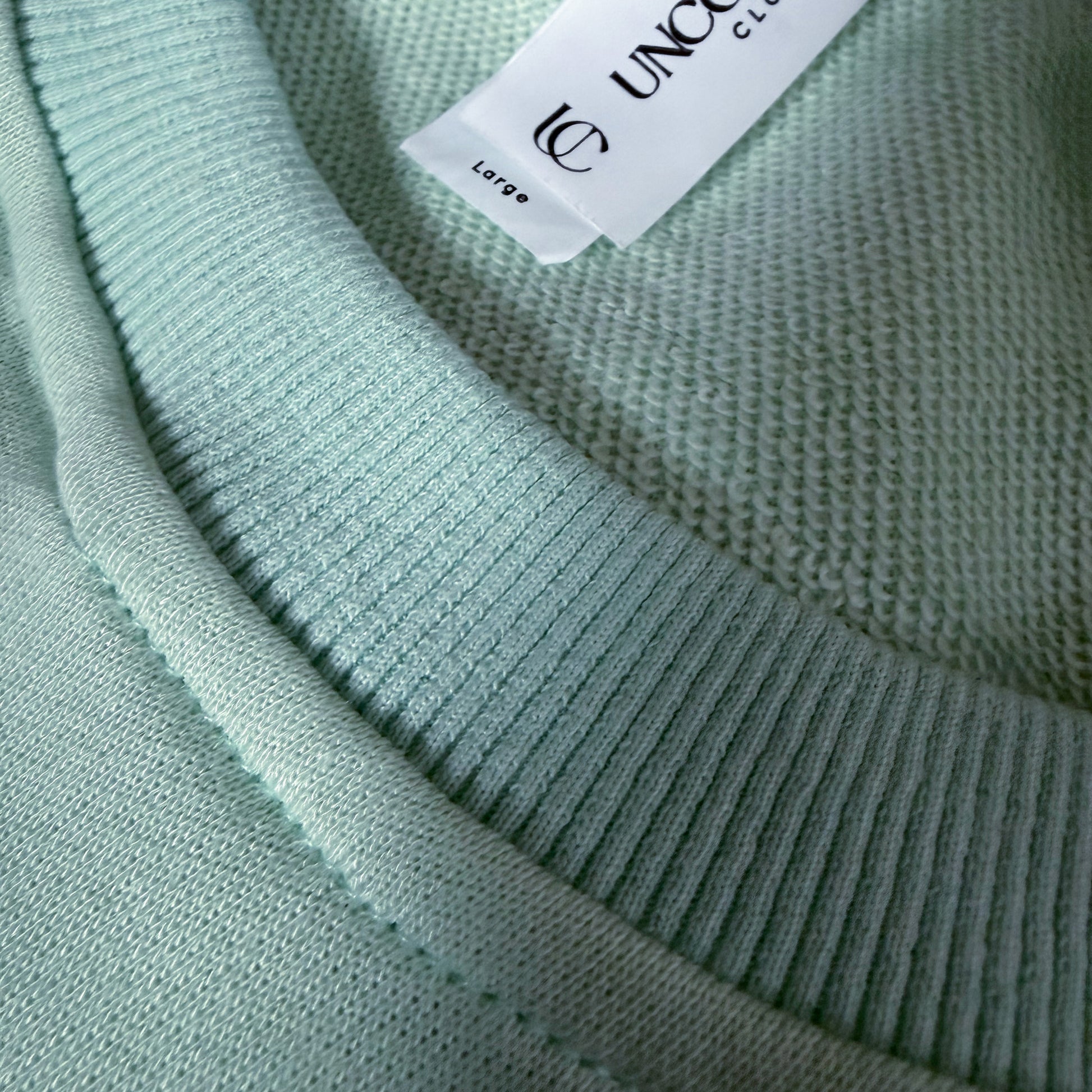 Close-up of a light green sweater with a brand tag on the collar.