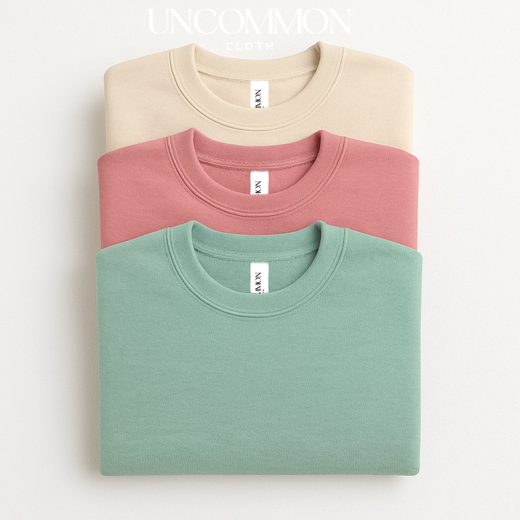 Three folded sweatshirts in beige, pink, and green on a white background with 'UNCOMMON cloth co' branding.